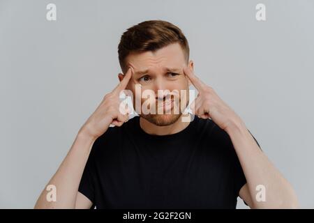 Besorgter Mann, der die Finger an Schläfen hält und denkt Stockfoto