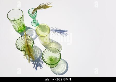 Sommerstill-Szene. Glitzernde grüne Gläser Wasser oder Cocktails auf weißem Tischhintergrund im Sonnenlicht. Lange harte Schatten. Urlaubskonzept Stockfoto