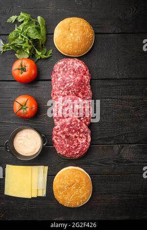 Hausgemachter Hamburger. Hacksteaks, Sesambrötchen mit anderen Zutaten, auf schwarzem Holztisch-Hintergrund, Draufsicht flach, mit Platz für Kopien Stockfoto