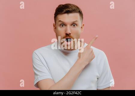 Schockierter junger Mann, der mit einem Finger zur anderen zeigt und einen überraschten Gesichtsausdruck zeigt Stockfoto