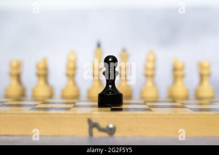 Schwarzer Bauer im Vordergrund, weiße Stücke im Hintergrund. Schachfiguren auf einem Schachbrett Seitenansicht. Stockfoto