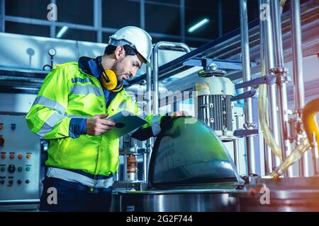 Werksingenieur, der in der Fabrik arbeitet und einen Tablet-Computer verwendet, um die Wartungsskessel-Wasserleitung in der Fabrik zu überprüfen. Stockfoto