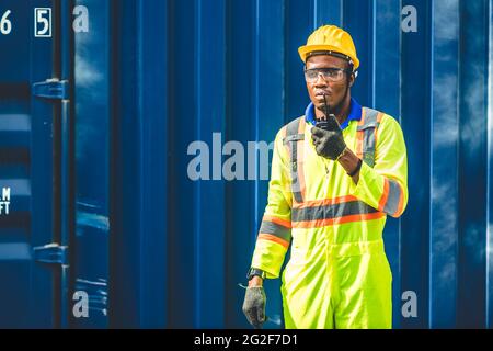 Schwarzer afrikanischer Arbeiter, der in der logistischen Schifffahrt Radio-Kontrolle Befehl Laden von Containern am Schifffahrtshafen arbeitet. Personal Fracht für Import Exportgüter Stockfoto