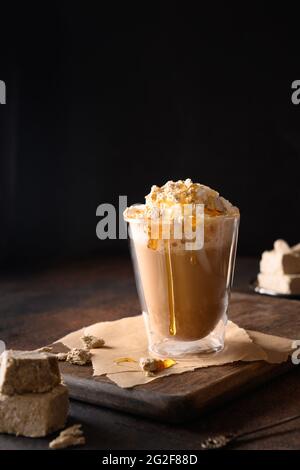 Leckerer Kaffee-Latte mit Halva-Garnitur Karamellsirup für Gourmet auf dunkelbraunem Hintergrund. Vertikale Ausrichtung. Stockfoto