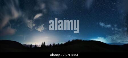 Herrlicher Panoramablick auf den nächtlichen Sternenhimmel über Nadelwald in den Bergen. Fantastische Landschaft von Bergwald mit Nadelbäumen unter blauem Himmel mit Sternen. Konzept der Nacht und Galaxie. Stockfoto