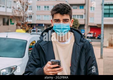 Junger Mann mit Telefon und Maske, der die Straße entlang läuft Stockfoto