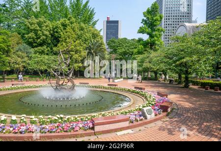 Tokio, Japan - 12.05.2019: Brunnen und Bäume im Hibiya Park im Zentrum Tokios mit Wolkenkratzern im Hintergrund an einem warmen, sonnigen Frühlingstag Stockfoto