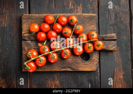 Kirschtomaten auf Ast, auf Holzschneidebrett, auf altem dunklen Holztischhintergrund, Draufsicht flach liegend Stockfoto