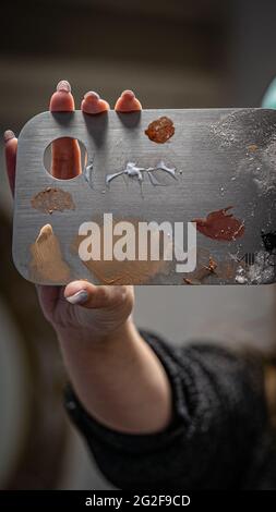 Nahaufnahme einer weiblichen Make-up-Künstlerin, die eine gebrauchte Edelstahl-Make-up-Mischpalette hält Stockfoto