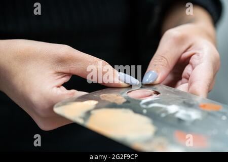 Nahaufnahme einer weiblichen Make-up-Künstlerin, die eine gebrauchte Edelstahl-Make-up-Mischpalette hält Stockfoto