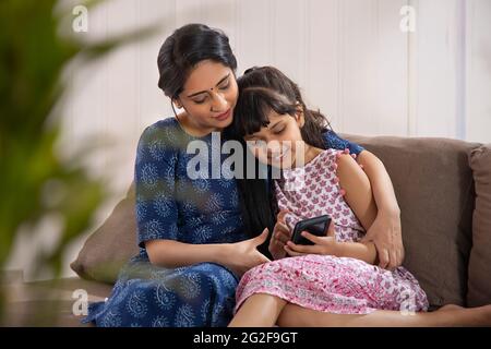 EINE JUNGE MUTTER UND TOCHTER NUTZEN GLÜCKLICH DAS HANDY Stockfoto