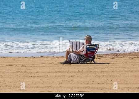 Mann, der an einem warmen, sonnigen Tag in Bournemouth, Dorset, Großbritannien, am Strand die Tageszeitung Daily Mail liest Stockfoto