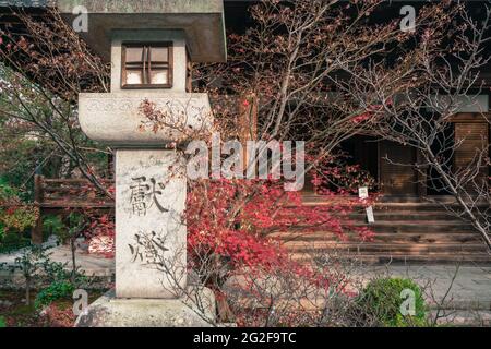 Eine Steinlampe vor einem alten, kleinen buddhistischen Schrein und einem kleinen japanischen Garten im Arashiyama-Viertel von Kyoto, Japan. Japanische Buchstaben Stockfoto