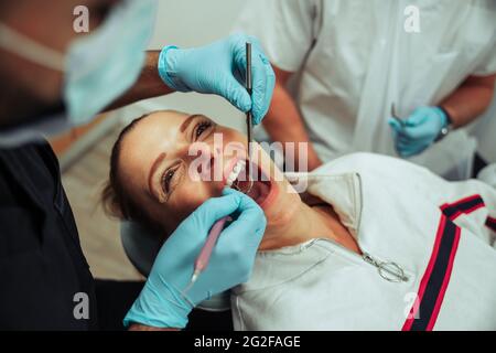 Kaukasische Frau liegt mit weit geöffnetem Mund, während eine Krankenschwester operiert Stockfoto
