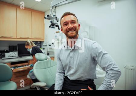 Hübscher kaukasischer Mann, der im Arztbüro steht, bereit für einen Termin mit einer Zahnärztin Stockfoto