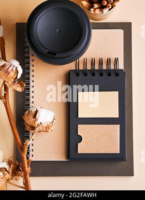 Branding-Mockup mit vielen Bastelpapier und Kaffee zu gehen in Kraftpapier Verpackung, umweltfreundliche Schreibwaren und Baumwolle Zweig. Schreibtisch mit einem Notizblock aus Papier und einer Schachtel mit Bleistiften. Modell. Stockfoto