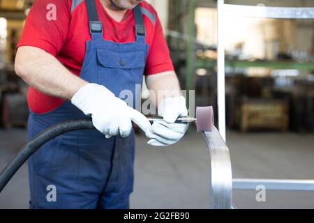 Arbeiter mit blauem Kragen, der ein Metallstück in einer Produktionsstätte poliert. Der Polierer arbeitet in einer Fabrik. Stockfoto