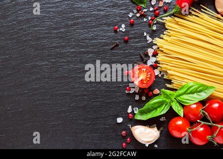 Tomaten, Spaghetti, Gewürze, Knoblauch und Basilikumblätter auf schwarzem Hintergrund. Italienisches Essen, Gesundheit oder Kochkonzept. Stockfoto