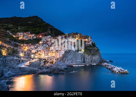 Lange Exposition von Manarola während der blauen Stunde. Lichter auf dem Meer. Stockfoto