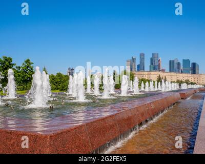 Jets von Springbrunnen an einem sonnigen Tag vor der Kulisse moderner Wolkenkratzer und einem wolkenlosen blauen Himmel. Erholungsgebiet im Victory Park auf Poklonnaya Stockfoto