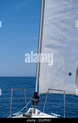 Weiße sloop manipulierte Yacht segelt im offenen, ruhigen Ozean, blauer Himmel im Hintergrund, sonniger Tag. Segelboot Deck, Bug, Mast und Segel Nahaufnahme. Freizeitaktivitäten Stockfoto