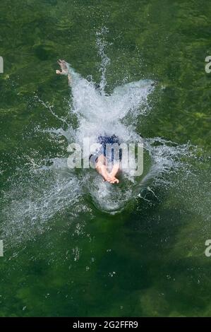 Dresden, Deutschland. Juni 2021. Ein Junge springt von einer hölzernen Fußgängerbrücke im Naturschwimmbad Mockritz ins Wasser. Die Freiluft-Badesaison wurde aufgrund von Corona mit einer Verzögerung im Freistaat eröffnet. Quelle: Sebastian Kahnert/dpa-Zentralbild/dpa/Alamy Live News Stockfoto