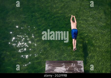 Dresden, Deutschland. Juni 2021. Ein Junge springt von einer hölzernen Fußgängerbrücke im Naturschwimmbad Mockritz ins Wasser. Die Freiluft-Badesaison wurde aufgrund von Corona mit einer Verzögerung im Freistaat eröffnet. Quelle: Sebastian Kahnert/dpa-Zentralbild/dpa/Alamy Live News Stockfoto