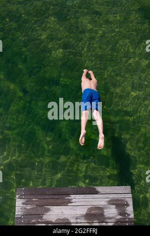 Dresden, Deutschland. Juni 2021. Ein Junge springt von einer hölzernen Fußgängerbrücke im Naturschwimmbad Mockritz ins Wasser. Die Freiluft-Badesaison wurde aufgrund von Corona mit einer Verzögerung im Freistaat eröffnet. Quelle: Sebastian Kahnert/dpa-Zentralbild/dpa/Alamy Live News Stockfoto