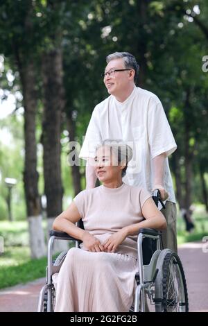 Der alte Mann schiebt seine Frau in einem Rollstuhl hochwertige Foto Stockfoto