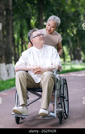 Der alte Mann schiebt seine Frau in einem Rollstuhl hochwertige Foto Stockfoto