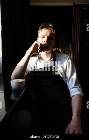 Porträt eines ruhenden jungen Mannes in weißem Hemd und Schürze. Helles Seitenlicht Stockfoto