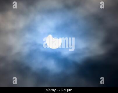 Partielle Sonnenfinsternis, wie sie in Glasgow Scotland am 10/06/2021 mit dramatischem Himmel und blauem Fleck durch die Sonne gesehen wurde. Stockfoto