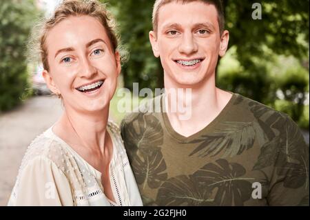 Horizontale Momentaufnahme eines jungen Paares, das im Freien posiert. Porträt eines lächelnden Mannes und einer Frau auf der Straße mit Zahnspangen. Kieferorthopädische Behandlung. Zahnpflegekonzept Stockfoto
