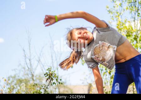 Defocus caucasian preteen Mädchen tun körperliche Bewegung im Park, Wald, im Freien, draußen. Schlanker Bauch. Gesunder Lebensstil. Übung zum seitlichen Biegen. Natur Stockfoto