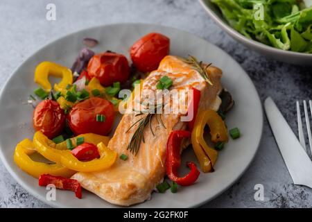 Gebackenes rotes Fischfilet Arctic Saibling auf einem Teller mit Gemüse, Salat in einer Schüssel mischen, leckeres herzhaftes gesundes Abendessen Stockfoto