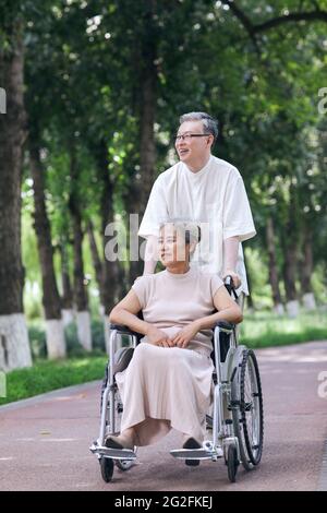 Der alte Mann schiebt seine Frau in einem Rollstuhl hochwertige Foto Stockfoto