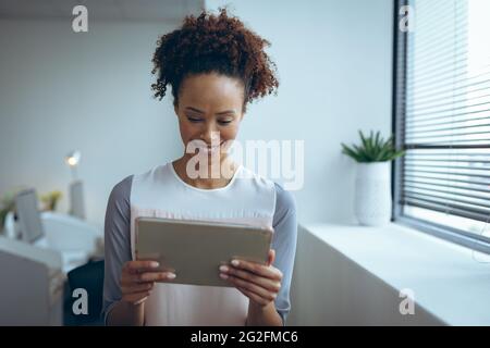 Eine Geschäftsfrau mit gemischter Rasse, die neben dem Fenster steht, lächelt und Tablet benutzt Stockfoto
