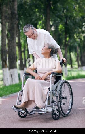 Der alte Mann schiebt seine Frau in einem Rollstuhl hochwertige Foto Stockfoto