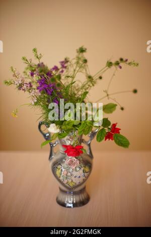 Bouquet von roten Rosen und wilden Blumen in einer Vase auf einem Holztisch. Stockfoto