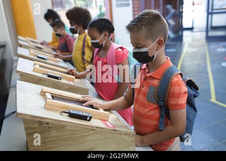 Eine Gruppe verschiedener Schüler, die in der Schule Gesichtsmasken mit digitalen Tablets tragen Stockfoto