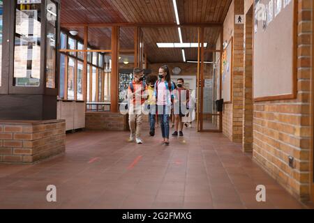 Eine Gruppe verschiedener Schüler, die Gesichtsmasken tragen, geht in der Schule durch den Flur Stockfoto