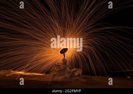 Fotografie aus Stahlwolle bei Nacht an der Felsstruktur der Wüste mit Feuerspritzern überall. Slow Shutter-Aufnahmen mit Stahlwolle Stockfoto