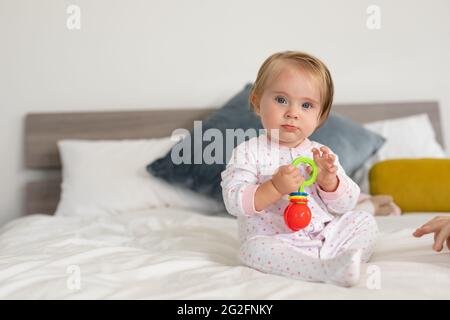 Porträt eines kaukasischen Babys, das mit einem Spielzeug spielt, während es zu Hause auf dem Bett sitzt Stockfoto