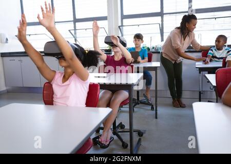 Eine Gruppe verschiedener Schüler, die in der Schule elektronische Geräte benutzen, während sie auf ihrem Schreibtisch sitzen Stockfoto