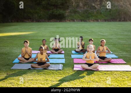 Eine Gruppe von verschiedenen Schülern, die Yoga praktizieren und meditieren, sitzt auf einer Yogamatte im Garten der Schule Stockfoto