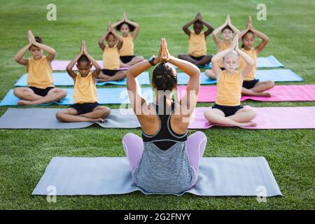 Eine Lehrerin und eine Gruppe verschiedener Schüler praktizieren Yoga und meditieren im Garten der Schule Stockfoto