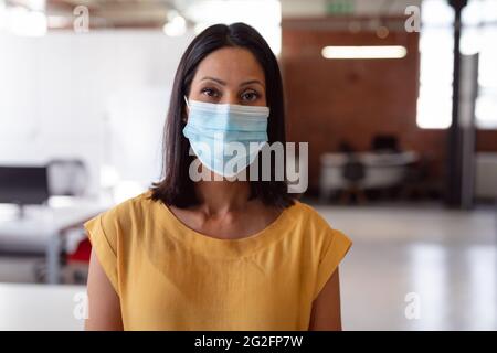 Porträt einer kaukasischen Geschäftsfrau mit Gesichtsmaske, die im Büro steht und direkt zur Kamera schaut Stockfoto