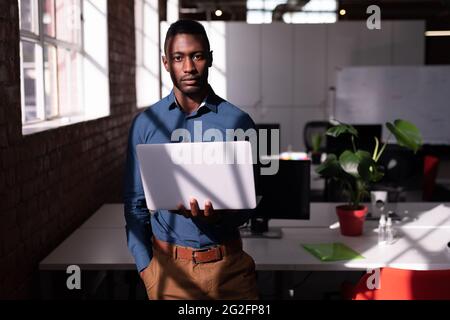 Porträt eines ernsthaften afroamerikanischen Geschäftsmannes, der im Büro mit einem Laptop steht Stockfoto