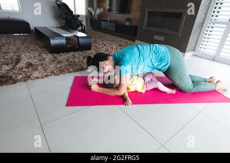 Kaukasische Mutter führt Plankenübungen durch, während das Baby zu Hause unter ihr liegt Stockfoto