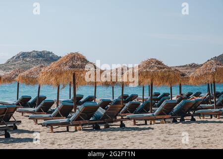 Kalafati, Griechenland - 23. September 2019: Blaue Sonnenliegen unter Sonnenschirmen am Strand von Kalafati, einem beliebten Strand auf Mykonos, der für Wassersport bekannt ist, an einem sonnigen Ort Stockfoto